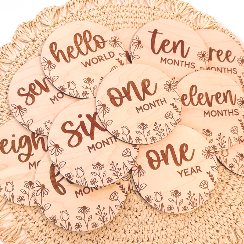 Floral wooden baby milestone discs arranged on neutral nursery background