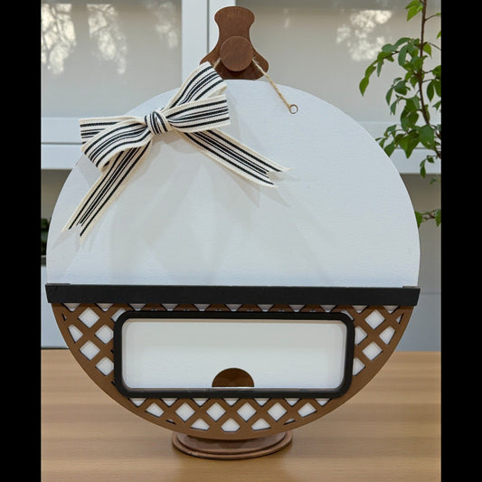 Unfinished round interchangeable door sign base made from layered wood, displayed unpainted with insert opening visible.