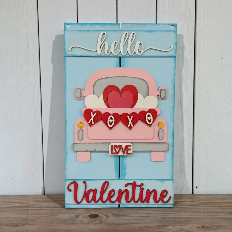 Decorative sign with a pink truck, hearts, and 'hello Valentine' text on a light blue background.