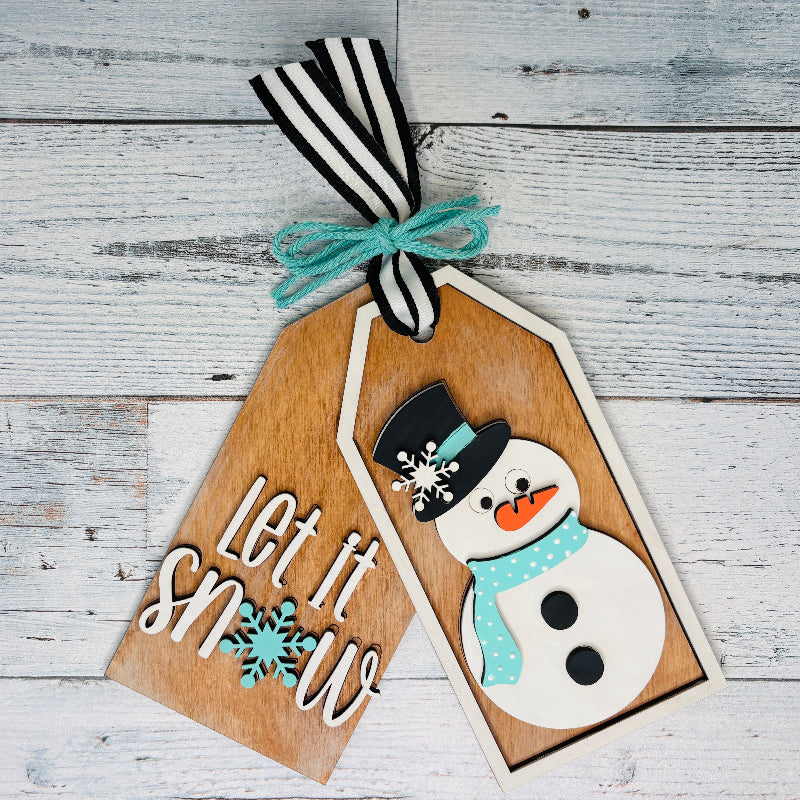 Wooden tag with snowman design and 'Let it Snow' text on a wooden surface craft kit at jazzis creations in orange park fl