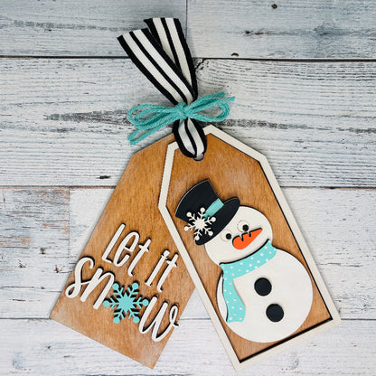 Wooden tag with snowman design and 'Let it Snow' text on a wooden surface craft kit at jazzis creations in orange park fl