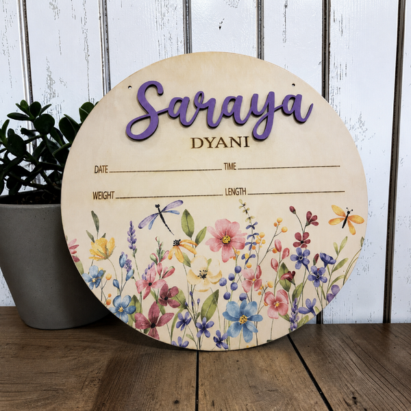 Personalized floral nursery birth announcement sign by Jazzi's Creations displayed in a neutral nursery, featuring 3D layered name lettering, colorful UV printed flowers, and engraved birth statistics.